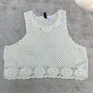 Vit virkad linnetopp från Divided - Superfin vit virkad linnetopp från Divided. Toppen är ärmlös med snyggt virkat mönster och rundade kanter. Nedtill finns dekorativa virkade cirklar som ger en boho-vibe. Perfekt för sommaren och lätt att styla till jeans eller kjol.