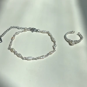 Smyckesset  - Setet innehåller: ✓ Ett handgjort armband ✓ En justerbar ring  Armband: Längd: 16,5 cm + 6,5 cm förlängningskedja Material: Rostfritt stål, äkta sötvattenspärlor   Ring: Justerbar storlek Material: Rostfritt stål 