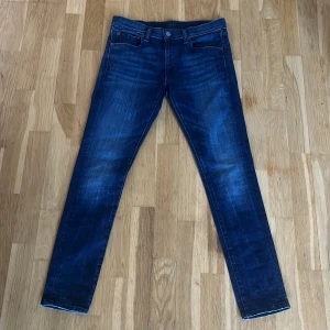 Mörkblå slim fit jeans Polo Ralph Lauren - Snygga mörkblå slim fit jeans från Polo Ralph Lauren med klassisk femficksdesign och diskreta slitningar. Jeansen har normal passform i midjan och smala ben, perfekta till sneakers eller boots. Materialet är mjukt och stretchigt jeans för extra komfort.