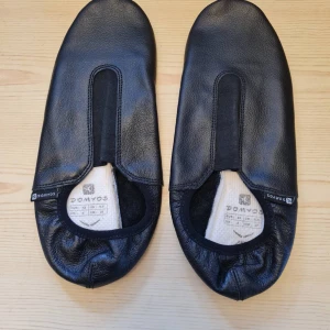 Svarta gymnastikskor i skinn strl 42 (Helt nya) - Säljer ett par helt nya svarta gymnastikskor i äkta läder som aldrig används. De har en enkel design med runt tå och elastisk öppning för enkel på- och avtagning. Perfekta för inomhusaktiviteter och träning. Storlek 42. Kan hämtas i Vallentuna.