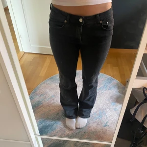 Svarta bootcut jeans med fickdetaljer! - Snygga svarta jeans med bootcut-modell och coola fickor bak med lock och knapp. Jeansen har normal passform och klassisk femficksdesign. Perfekta för dig som vill ha en tidlös look med lite edge.