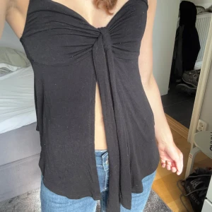 Svart knyttopp från Gina Tricot  - Supersnygg svart linnetopp från Gina Tricot i storlek XS. Toppen har smala axelband (ej justerbara), knytdetalj framtill och en lätt flowy passform. Perfekt att styla med jeans för en trendig look. Tyget är väldigt stretchigt och skönt. Kommer ej till användning längre!💕