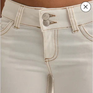 Vita jeans Nelly - Snygga vita jeans med bruna kontrastsömmar. Låg midja, dubbla silverknappar och klassiska bakfickor med coolt broderat mönster. Perfekta för en clean och fräsch look. I bra skick används fåtal gånger. Lite slitage längst ner på benet 