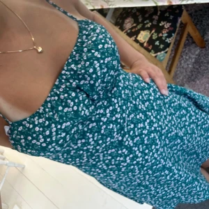 Grön blommig kortklänning  - Supersöt grön kortklänning med vita småblommor och smala axelband som knyts på axlarna. Klänningen har en lätt utställd passform och är perfekt för varma dagar. Säljer den billigt speciellt pga att den är från shein men kvaliteten är ändå bra.