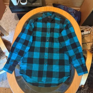 Blå och svart rutig skjorta från GAP - Snygg blå och svart rutig skjorta från GAP i 100% bomull. Skjortan har klassisk krage, knäppning framtill och en bröstficka. Perfekt för dig som gillar en avslappnad men ändå stilren look.