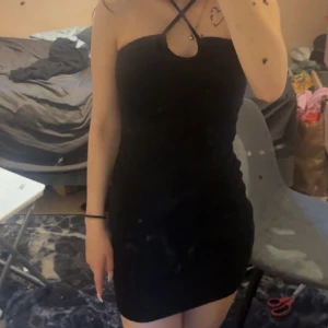 Svart kort klänning med halterneck - Säljer en svart kort klänning med halterneck och kryssade band framtill. Klänningen är tight och har en snygg struktur i tyget som ger en cool känsla. Perfekt för dig som gillar minimalistisk stil med en twist. Näst intill oanvänd, pris för fler bilder och pris kan diskuteras 💓🥰