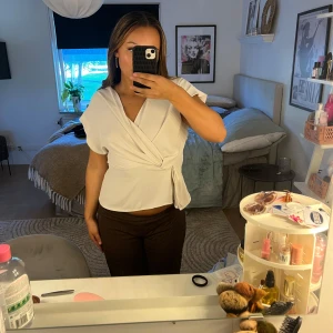 Vit omlottopp med knyt i midjan - Säljer en vit omlottopp med knyt i midjan och v-ringad hals.. Perfekt att styla med jeans eller kjol. Tröjan har spruckit lite i armvecket men de är inget man tänker på och de går lätt att sy igen💕