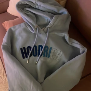 Ljusblå HOODRICH hoodie med brodyr - Snygg ljusblå hoodie från HOODRICH med broderad logga i olika blå nyanser och vitt framtill. Tröjan har huva med snörning. Går inte att få tag på denna modell som ny!! 