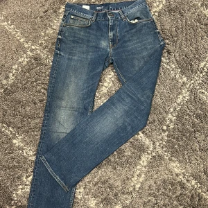 Blå jeans från Tommy Hilfiger - Snygga blå jeans från Tommy Hilfiger med klassisk femficksdesign och diskret logga på bakfickan. Jeansen har normal passform och raka ben, tillverkade i mjukt denimtyg. Perfekta för en avslappnad och stilren look.