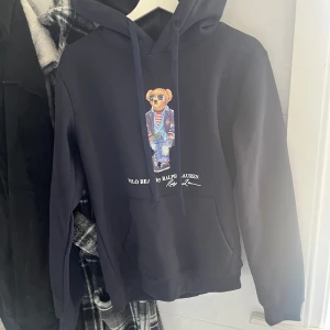 Svart Polo Bear hoodie från Ralph Lauren - Svart hoodie från Ralph Lauren med ikoniska Polo Bear-trycket framtill. Ny pris 2700
