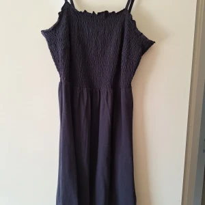 Mörkblå kort klänning från bpc - Supersöt mörkblå kort klänning från bpc med smockad överdel och tunna axelband. Klänningen har en lätt utställd kjol och är perfekt för varma dagar. Tillverkad i mjuk bomull som känns skön mot huden.
