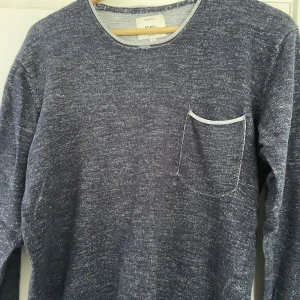 Mörkblå långärmad tröja Rebel XL - Mörkblå långärmad tröja från Rebel i storlek XL. Tröjan har en melerad look med en bröstficka och ljusa sömmar vid halsringning och ficka. Perfekt för dig som gillar en avslappnad och stilren vibe.