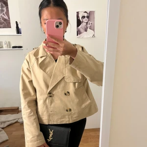 Snygg cluth  - Säljer en beige skepparkavaj med dubbelknäppning och stora slag. Jackan är croppad och har axelklaffar för en cool look. Tillverkad i bomull, perfekt för lager-på-lager under vår och höst. Enkel att styla med både jeans och kjol.