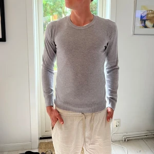 Ljusgrå stickad tröja från Marnello - Snygg ljusgrå stickad tröja i viskos från Marnello i klassisk modell. Tröjan har rund halsringning, ribbade muddar och lång ärm. Perfekt för lager-på-lager och enkel att matcha med olika outfits.