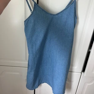 Ljusblå jeansklänning från Rockorie - Supersöt ljusblå jeansklänning från Rockorie i storlek XS. Klänningen har smala axelband och är ärmlös med en enkel, rak passform. Perfekt för varma dagar och lätt att styla med sneakers eller sandaler.