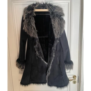 70s Faux fur vintage coat - Säljer en svart kappa med grå fuskpäls runt krage, ärmslut och nederkant. Kappan har snygga hornknappar och vanliga knappar men en av hornknapparna har gått av.