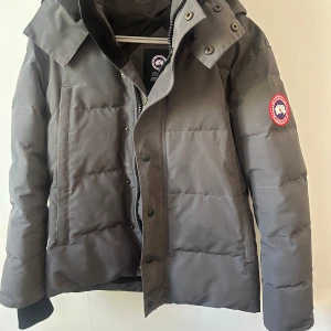 Canada goose Jacka  - Säljer en grå jacka från Canada Goose i storlek XS men passar S-M. Jackan har avtagbar huva med pälsdetalj, klassisk logga på ärmen och dragkedja med tryckknappar. Perfekt för kalla vinterdagar och riktigt snygg streetstil.