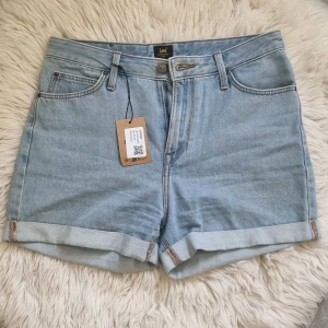 Ljusblå jeansshorts från Lee - Snygga ljusblå jeansshorts från Lee med klassisk femficksdesign, uppvikta benslut och detaljerade sömmar. Shortsen har bälteshällor, knapp och dragkedja framtill samt Lee-logga på både knapp och bakficka. Perfekta för varma dagar.