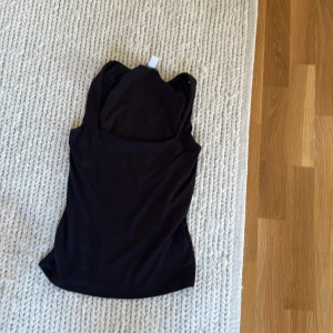 Svart ärmlös linnetopp - Aldrig använd. En stilren svart linnetopp med ärmlös design och rundad hals. Perfekt att matcha med jeans eller kjol för en clean look. Tunt och mjukt material som känns skönt mot huden. 