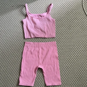 Ribbad rosa linnetopp och shorts från Primark - Säljer en ribbad rosa linnetopp samt tränsingsshorts från Primark med smala axelband och croppad passform. Toppen och shortsen är i stretchigt material och har en ljusrosa ton som känns fräsch till sommaren. Settet är perfekt till en joggingtur, promenad eller en avslappnad kväll hemma.