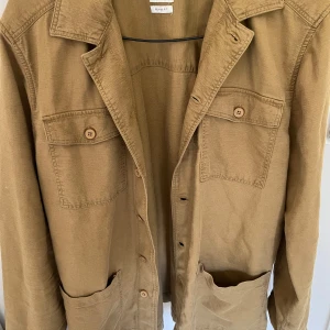 Beige overshirt från ZARA, relaxed fit - Snygg beige overshirt från ZARA i relaxed fit. Jackan har två bröstfickor med knappar och stora fickor framtill. Perfekt lager-på-lager-plagg med klassisk krage och knappstängning. Skön och stilren att slänga på över en hoodie eller t-shirt.