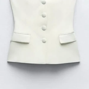 Vit omlottväst med stora knappar - Snygg vit topp med omlott-design och stora klädda knappar framtill. Toppen har en v-ringad hals och markerad midja, samt två fickdetaljer framtill. Perfekt att styla med matchande byxor för en clean och modern look. Jag skulle säga att den passar för dig som vanligtvis är XS/S. Toppen har använt fåtal gånger och ser percis ut som ny. Toppen köptes för 400kr men kommer säljas för 350kr