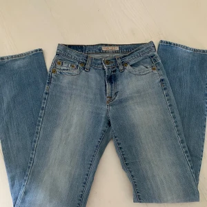 Ljusblå bootcut/straight  jeans Holiday - Ljusblå jeans från Holiday Jeans Company med straight passform. Klassisk femficksmodell, snygga slitningar och detaljer i mässing. Tillverkade i bomull med lite stretch för extra komfort. Perfekta för en avslappnad och trendig look.