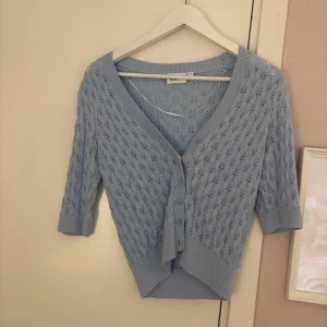 Ljusblå stickad kofta från Kappahl - Supersöt ljusblå stickad kofta från Kappahl i croppad modell. Koftan har v-ringning, fina knappar framtill och ett diskret hålmönster. Ärmarna är trekvarts och materialet känns mjukt och luftigt, perfekt för vår och sommar.