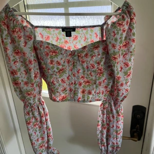 Blommig croppad blus från Boohoo - Supersöt blommig blus från Boohoo i ljusblått med rosa och gröna blommor. Croppad modell med långa puffärmar och resår vid ärmslut och axlar. Perfekt för dig som vill ha en somrig look!
