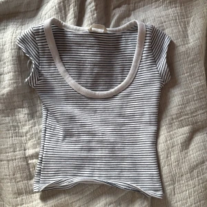 Randig croppad topp med rund hals - Snygg croppad topp med smala svarta ränder på vit botten och bred rund halsringning. Kortärmad och i mjukt bomullsmaterial, perfekt till jeans eller kjol för en chill look.