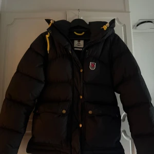 Svart Fjällräven Expedition dunjacka - Svart Fjällräven Expedition Series dunjacka med gula snören och guldiga knappar. ‼️‼️Kan även byta till en svart fast i storlek s‼️‼️
