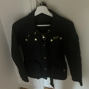 Svart Barbour jacka med guldiga detaljer  - Säljer en svart Barbour jacka med snygga guldiga knappar och dragkedja. Säljer för att den inte kommer till använding och har blivit för liten, har änvänt den två gånger och kände att den bara inte var för mig, köpte den för 5500 och säljer för 2000 pris kan diskuteras 