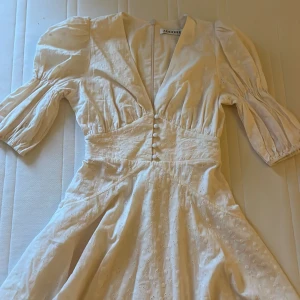 Beige kortklänning från Adoore - Supersöt beige kortklänning från Adoore med puffiga trekvartsärmar och v-ringad hals. Klänningen har broderade detaljer, knappar framtill och markerad midja. Tillverkad i bomull, perfekt för sommarens alla tillfällen. Snygg och feminin siluett! Säljer då den är för liten (därför ingen bild på)🫶🏻