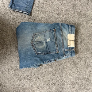 Tiger of Sweden ljusblå jeans W32 L34 - Säljer ett par jeans i ljusblå tvätt med slitningar och snygga detaljer på fickorna. Modellen har rak passform och klassisk femficksdesign. Perfekt för dig som gillar en avslappnad och cool stil.