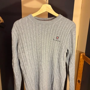 Ljusgrå kabelstickad tröja Bondelid - Säljer en ljusgrå kabelstickad tröja från Bondelid med broderad logga på bröstet. Tröjan har rund halsringning och långa ärmar. Perfekt för dig som gillar klassisk och stilren look. Materialet är mjukt och skönt mot huden.