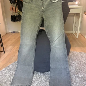 Grå bootcut jeans från Gina Tricot - Snygga grå jeans från Gina Tricot i bootcut-modell, i storlek 170 men är som en S. Jeansen har låg midja, knäppning med tre silverfärgade knappar och klassiska bakfickor. Materialet är mjukt denim och färgen är tvättad grå med lätt slitning för en cool look. Inga defekter !!! Kontakta mig om du har några funderingar!!❤️
