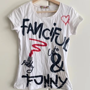 Vit t-shirt med tryck från Replintext - Vit t-shirt från Replintext med coolt grafiskt tryck i svart och rött framtill, inklusive text, hjärta och läppstift. Rund hals och korta ärmar. Materialet är mjuk bomull och passformen är slim. Perfekt för dig som gillar statement-plagg.