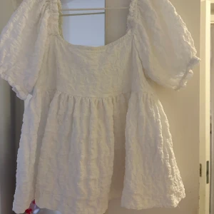 Vit blus med puffärm från Gina Tricot - Supersöt vit blus från Gina Tricot i storlek 146/152. Blusen har puffiga korta ärmar, en fyrkantig ringning och ett vågigt, strukturerat tyg som ger en unik look. Perfekt för dig som gillar romantiska och luftiga plagg. Ett litet hål under bröstet som knappt syns, se sista bilden💓