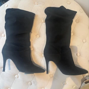 Svarta höga stövletter med klack - Snygga svarta stövletter i mocka-look med spetsig tå och hög klack. Skorna har en slouchy passform som ger en cool och trendig vibe. Perfekta att styla med jeans eller kjol för en edgy look.
