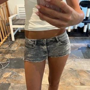 Grå slitna jeansshorts med rå kant - Supersnygga grå jeansshorts med tvättad look och rå, fransig kant nertill. Modellen är lågmidjad och har klassiska fickor både fram och bak samt bälteshällor. Perfekta för varma dagar när du vill ha en edgy vibe.