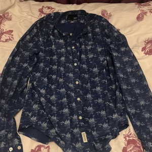 Blå blommig skjorta  - Säljer en blå skjorta från lager 157. Skjortan har långa ärmar och vita knappar framtill. Hör av dig vid intresse!!!😆