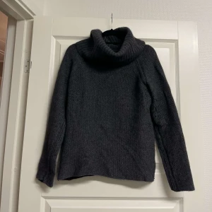 Tröja  Peak Performance L - Mysig mörkgrå polotröja från Peak Performance i storlek L. Stickad i ull med grov struktur och hög, bred polokrage. Perfekt för kalla dagar och enkel att matcha med jeans eller kjol. Långärmad och klassisk passform.