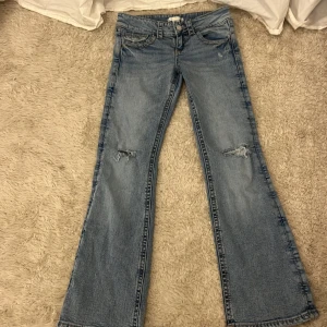Bootcut jeans från Gina Tricot, blå använda minst två gånger super fint skick perfekta nu till hösten - Bootcut jeans från Gina Tricot i ljusblå tvätt med slitningar på knäna. Klassisk femficksmodell med snygga detaljer på bakfickorna och silverfärgade knappar. Jeansen har låg midja och är tillverkade i bomull för en skön känsla.