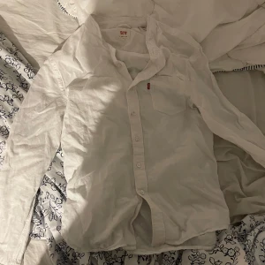 Vit skjorta från Levi's i bomull - Klassisk vit skjorta från Levi's i mjuk bomull. Skjortan har lång ärm, bröstficka med den ikoniska röda Levi's-taggen och knäppning framtill. Perfekt för en clean och stilren look.