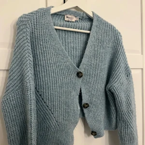 Ljusblå stickad kofta från NA-KD - Supermysig ljusblå stickad kofta från NA-KD med grov ribbad struktur. Koftan har v-ringning, tre stora knappar framtill och lång ärm. Perfekt att slänga över en t-shirt eller linne för en chill look.