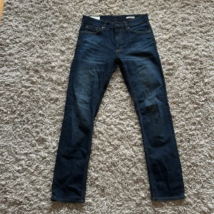 Mörkblå jeans från GANT - Snygga mörkblå jeans från GANT med klassisk femficksdesign och raka ben. Jeansen har en stilren läderpatch med GANT-logga bak i midjan och kontrastsömmar. Perfekta för dig som gillar en tidlös och clean look.