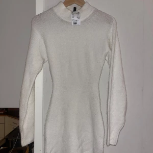 Vit stickad kortklänning H&M - Supermysigs vit stickad klänning från H&M med lång ärm och hög krage. Den har en liten slits. Klänningen är figurnära och har en enkel, stilren design som passar perfekt till kyligare dagar. Perfekt att styla med boots eller sneakers.