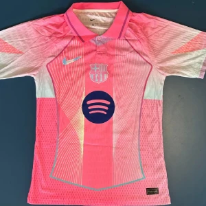 Barcelona Lamine Yamal #10 rosa matchtröja - Snygg helt ny, oanvänd, Barcelona fotbollströja från Nike i en ljusrosa ton med vita och mörkblå detaljer. Tröjan har korta ärmar, krage och tryck med Spotify-logga samt klubbmärke på bröstet. På ryggen står Lamine Yamal och nummer 10 i mörkblått. Materialet är lätt och ventilerande polyester. Skriv till mig innan ni köper.