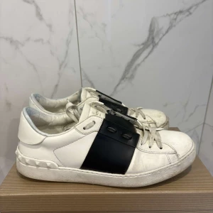Valentino open  - Snygga vita sneakers från Valentino med en bred svart rem över snörningen. Skorna har en rund tå och en stilren design som passar perfekt för en trendig look.