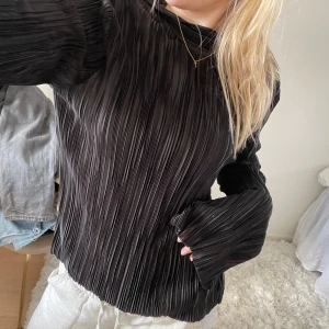 Svart plisserad blus - Snygg svart plisserad blus med långa ärmar. Perfekt för en stilren look. Blusen har en elegant struktur och en bekväm passform.